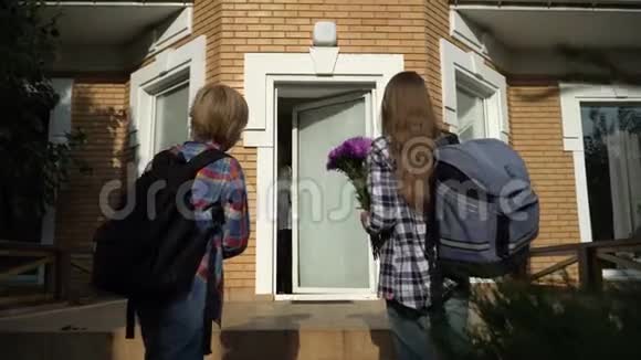 小可爱的男孩和女孩带着背包回家给他们的母亲带花幸福的家庭观念视频的预览图