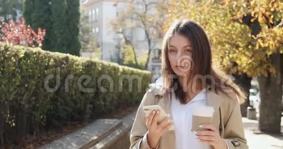 年轻英俊的泼妇在历史悠久的绿色城市中走来走去端着杯子喝热咖啡视频的预览图