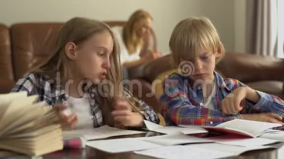 可爱的弟弟和妹妹在家学习的前景而他们的母亲坐在后台视频的预览图