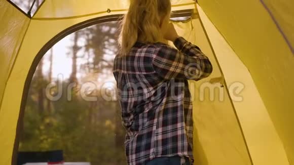 少女在阳光明媚的森林里打开窗户露营帐篷在黄色露营帐篷里的年轻旅游女孩在森林徒步旅行视频的预览图