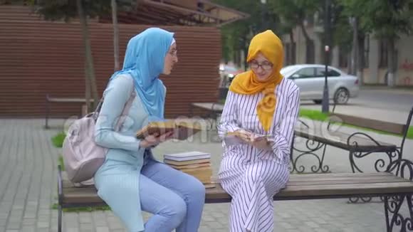 两名戴着传统围巾手里拿着课本的穆斯林女学生在公园里近距离交流视频的预览图