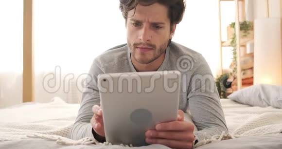 一个在床上用数码平板电脑的糊涂男人视频的预览图
