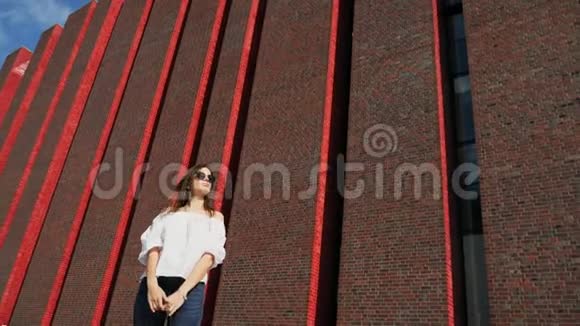 幸福美丽的女人站在城市街道上靠近一座现代化的砖楼展览中心视频的预览图