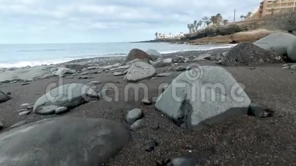 4k摄像机在黑色火山沙和大洋海滩上的大岩石上飞行视频的预览图
