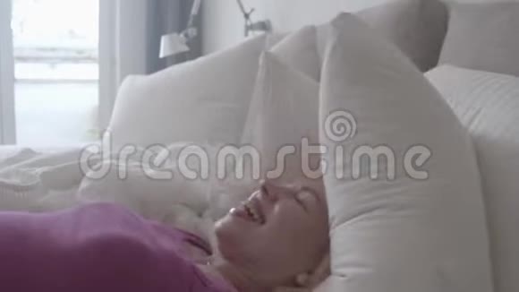 爱笑的年轻女子在家里躺在床上枕头上动作缓慢视频的预览图
