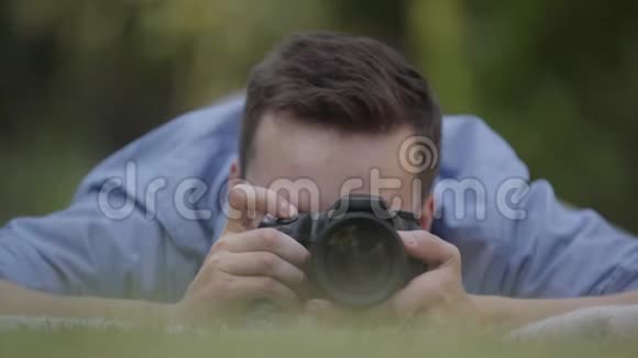 年轻的职业男性摄影师在草地上用相机拍照的肖像摄影专业视频的预览图