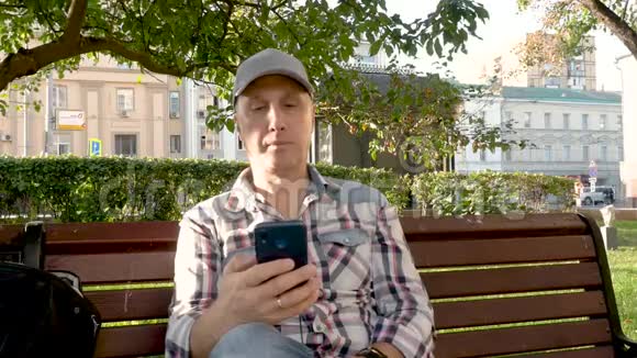 白种人坐在公园里坐在长凳上听耳机音乐视频的预览图