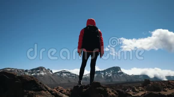 带着黑色背包的年轻女子徒步旅行者呆在山顶上对抗蓝天和云彩慢动作视频的预览图