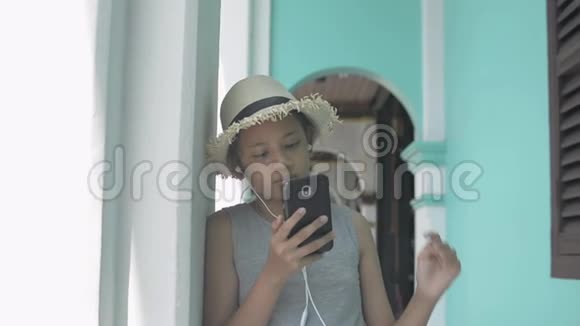 亚洲可爱的女孩穿着休闲装戴着草帽用手机和耳机站在街机旁视频的预览图
