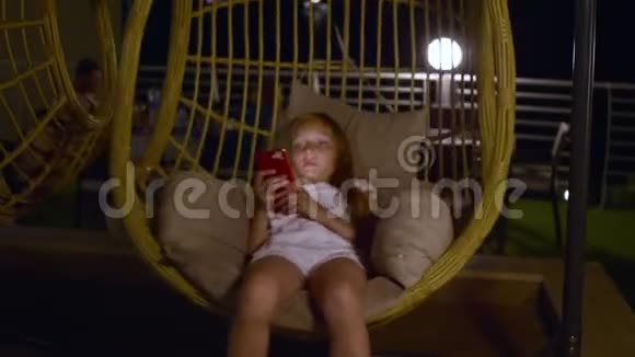 可爱的少女使用智能手机在摇茧椅上休息视频的预览图