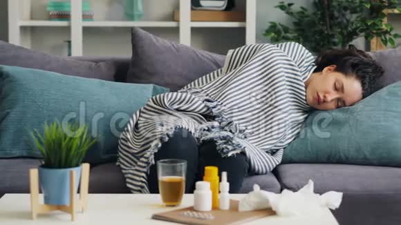 生病的年轻女士在温暖的毯子下睡在沙发上放松视频的预览图