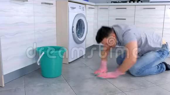 不高兴的疲惫的男人戴着橡胶手套在厨房里用力地洗和摩擦地板坐在地板上侧视视频的预览图