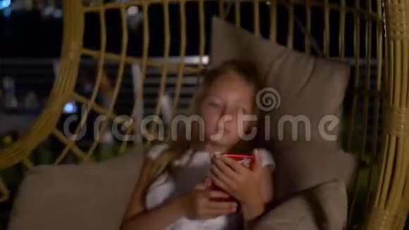 十几岁的女孩在茧柳条椅上摇摆看着智能手机少女晚上使用手机视频的预览图