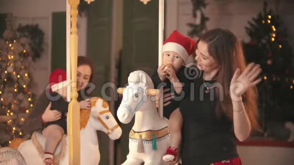 圣诞节概念两个婴儿坐在旋转木马马室内玩他们的母亲抱着他们视频的预览图