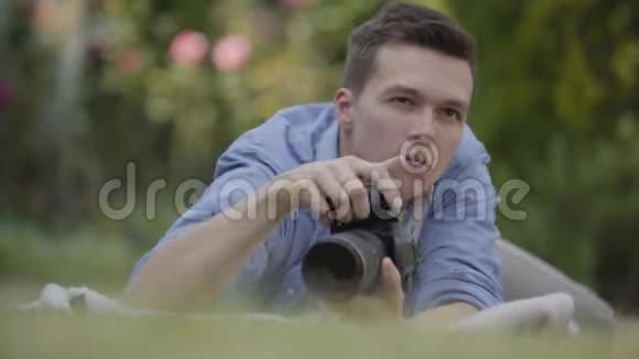 年轻的职业男性摄影师用相机躺在草地上微笑拍照的肖像视频的预览图