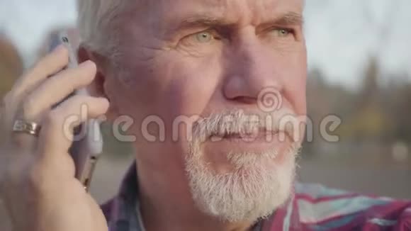 一个成熟的白人男子站在秋天的公园里用智能手机说话高级欧洲球员视频的预览图