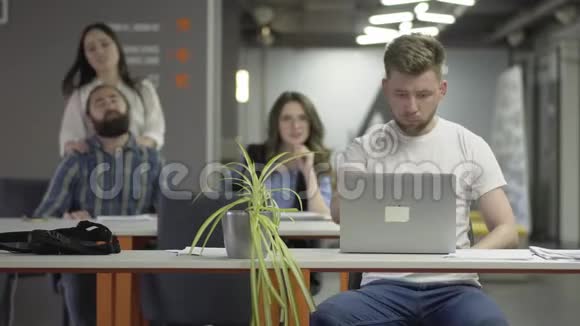 这位穿着白色t恤的专心致志的年轻人用笔记本电脑完成了他的工作然后在办公室里走开了男人和视频的预览图