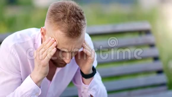 不高兴的休闲男性头痛按摩太阳穴坐在夏季公园的长凳上中等特写视频的预览图