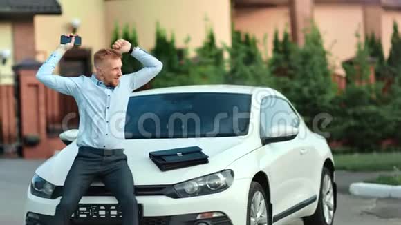 快乐的成功的年轻商业男性胜利者的姿态举起手坐在车盖上视频的预览图