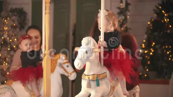 圣诞节装饰工作室两个微笑的母亲与他们的婴儿坐在旋转木马上玩视频的预览图