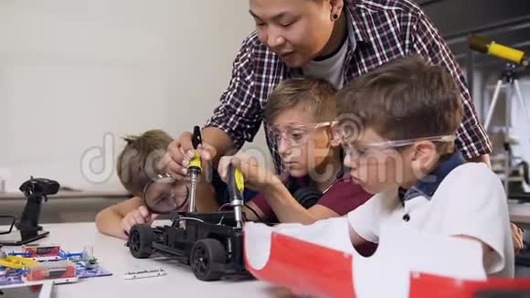 机械工程师帮助男孩使用螺丝刀在现代舒适的桌子上组装机器人机器视频的预览图
