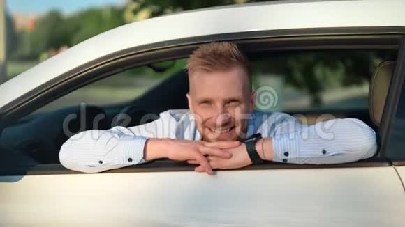 一幅英俊的男性商人在白色豪华跑车上摆姿势透过敞开的窗户看的画像视频的预览图