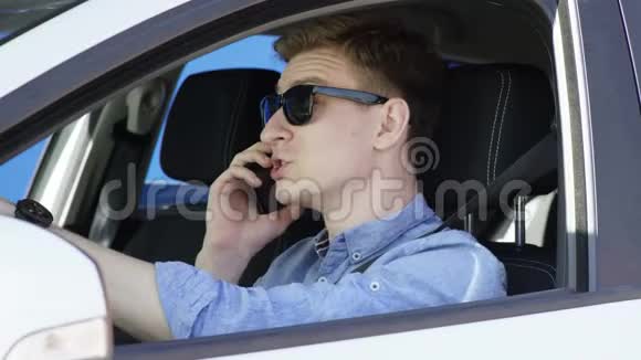在智能手机上发言的年轻人坐在他的白色汽车上带着布鲁斯的背景感到欣喜若狂他是视频的预览图