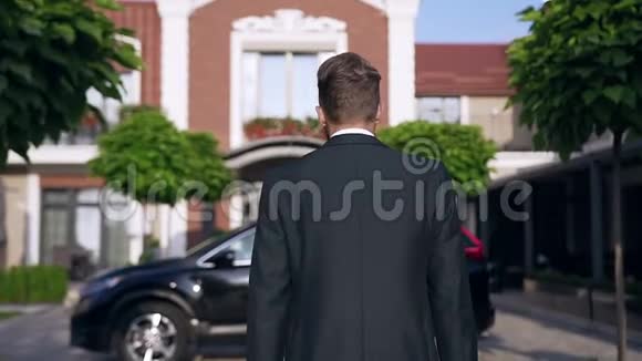 苗条英俊的商人走着坐在黑色的汽车旁站在漂亮的房子旁慢悠悠地走着视频的预览图
