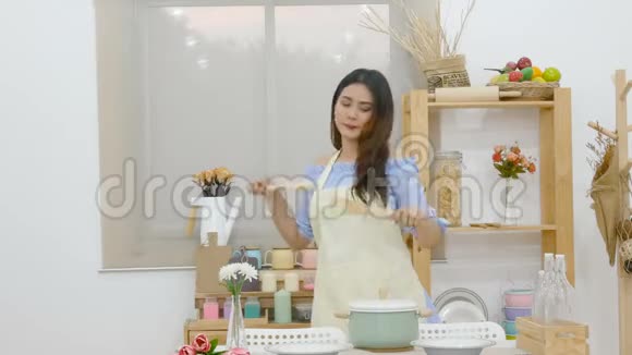 4K美丽的亚洲女人拿着瓢在厨房里跳舞喜欢在餐桌后面用锅做饭视频的预览图