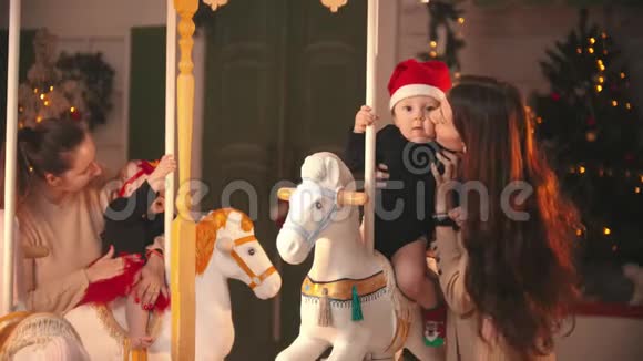 圣诞节概念两个婴儿坐在旋转木马上他们微笑的母亲站在他们身边抱着他们视频的预览图