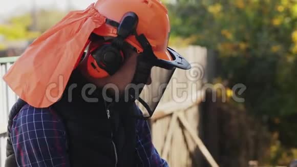 一个戴头盔的伐木工人用电锯砍木头视频的预览图