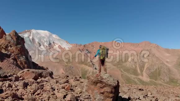 徒步旅行者背着背包站在山上的一块大石头上视频的预览图