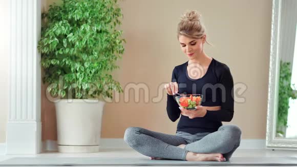 微笑健身妇女坐在莲花的位置用叉子吃新鲜蔬菜沙拉视频的预览图