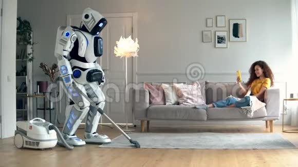 当一个女孩躺在沙发上时一个机器人做真空清洁Cyborg和人类概念视频的预览图