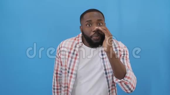 非洲裔美国男子一头非洲发穿着t恤站在孤立的蓝色背景上要求安静视频的预览图