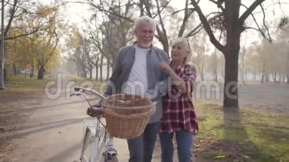 在雾蒙蒙的公园里一对快乐的白人夫妇骑着自行车沿着小巷散步退休的成熟家庭开支视频的预览图