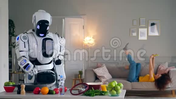 Cyborg和人类概念白色机器人做饭而女人则玩智能手机视频的预览图