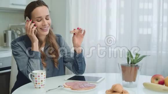 微笑的女人在电话里说话家庭主妇在家吃sadwich和咖啡视频的预览图