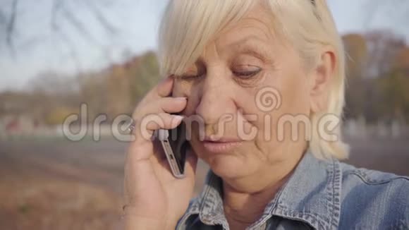 成熟的欧洲女人站在秋天的公园里用智能手机说话积极的高加索人视频的预览图