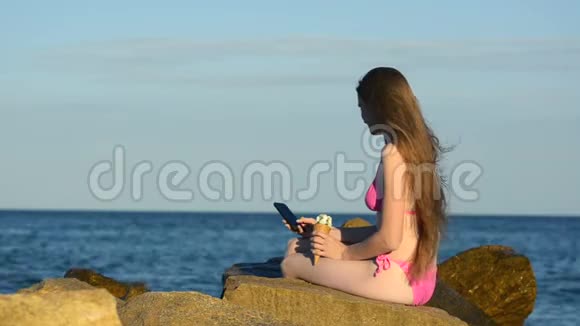 长发少女端着冰淇淋坐在沙滩上打电话拍照视频的预览图