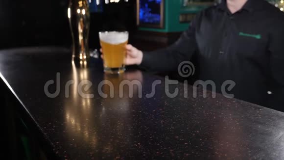 酒保在黑暗的酒吧柜台上拿着装满啤酒的杯子的特写镜头啤酒杯被送到视频的预览图