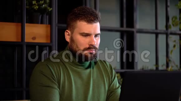 一个长胡子的野蛮男人坐在咖啡馆里用笔记本电脑工作视频的预览图