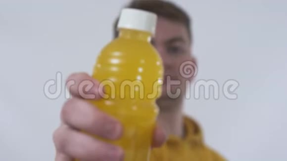 一个年轻人的特写镜头提出一个装有橙汁的瓶子把它放在摄像机旁边摄影棚视频的预览图