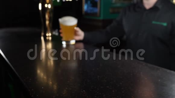 酒保在黑暗的酒吧柜台上拿着装满啤酒的杯子的特写镜头啤酒杯被送到视频的预览图