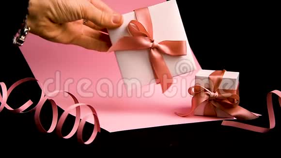 女性手在粉红色和黑色背景上放置粉红色丝带的礼物盒视频的预览图