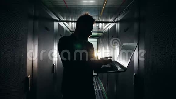 一个IT工人的剪影在黑暗的服务器单元里有一台笔记本电脑信息技术工程师在服务器机房工作视频的预览图
