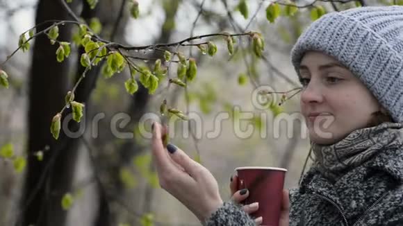 手里拿着纸杯的年轻女子触摸着一片盛开的绿叶潮湿的雪视频的预览图