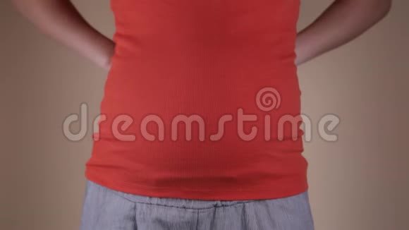 一个穿着红色T恤的孕妇腹部的特写镜头她手里拿着两张写有文字的床单视频的预览图