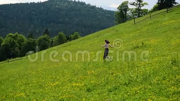 年轻女子沿着一片青山草地奔跑晴朗的夏日远处的森林和山脉慢动作视频的预览图