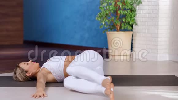 瑜珈年轻女子放松练习瑜珈抬腿从一边到另一边躺在垫子上视频的预览图